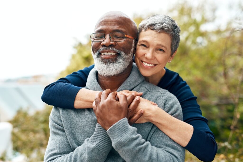 Woman in blue shirt hugging man in grey sweater outside by a tree